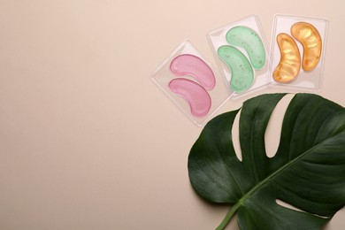 Under eye patches and tropical leaf on beige background, flat lay with space for text. Cosmetic product