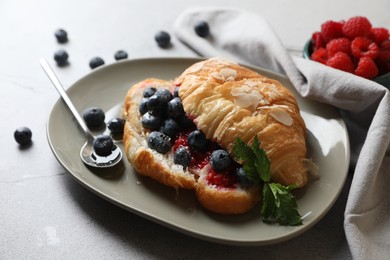 Photo of Delicious croissant with berries, almond flakes and spoon on light grey table