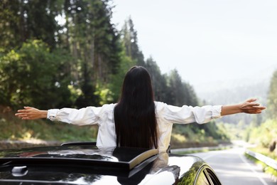 Photo of Enjoying trip. Woman leaning out of car roof outdoors, back view