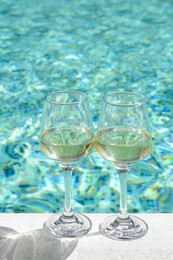 Photo of Glasses of tasty wine on swimming pool edge