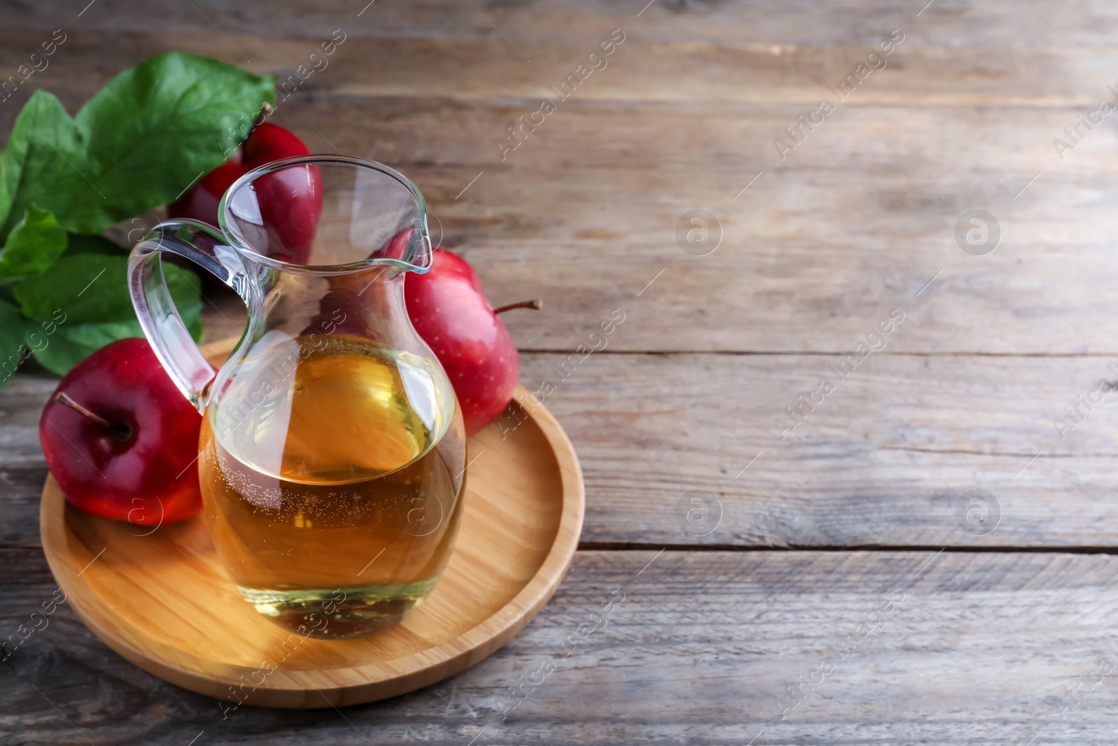 Photo of Jug of tasty juice and fresh red apples on wooden table, space for text