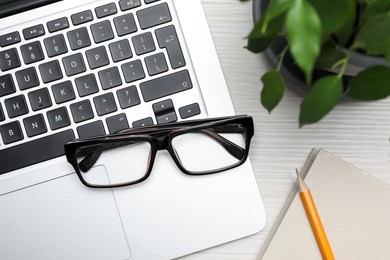 Modern laptop, pencil, glasses and houseplant on white wooden table, flat lay