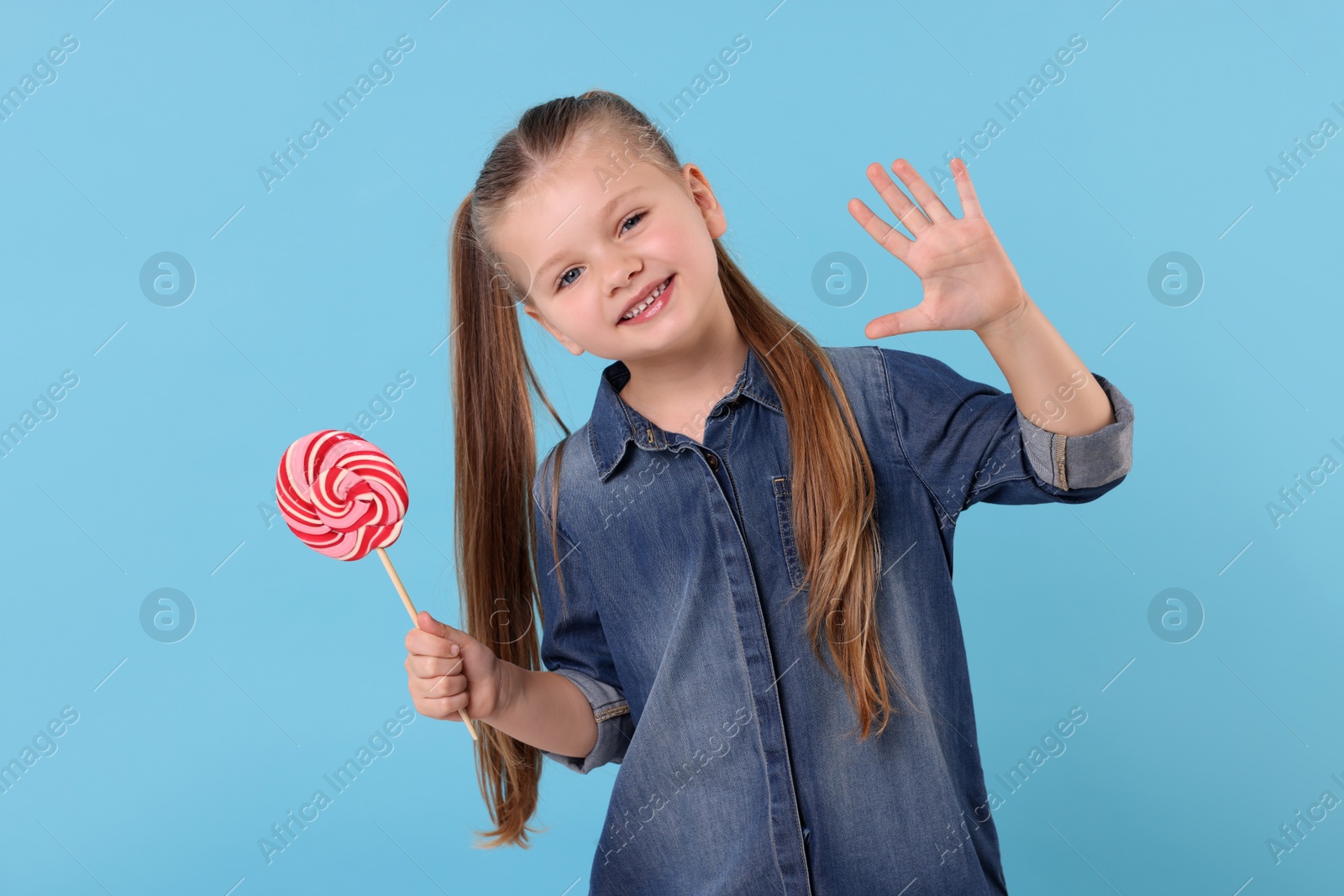 Photo of Happy little girl with bright lollipop swirl on light blue background