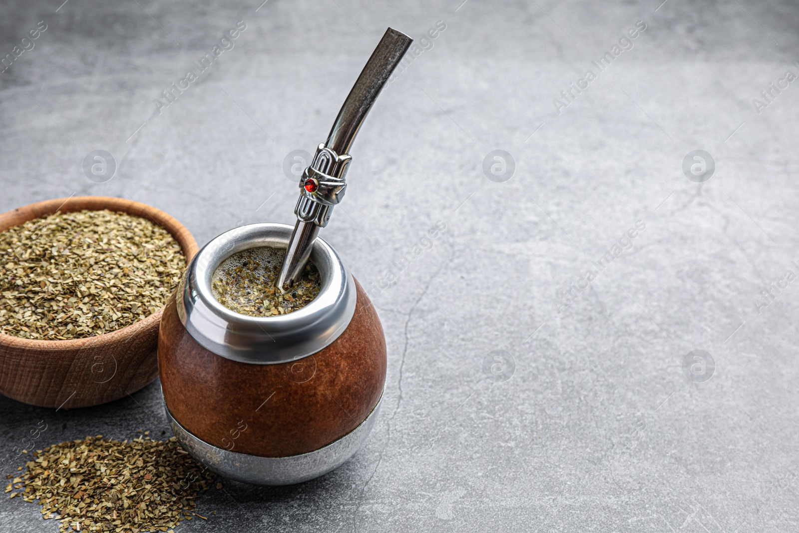 Photo of Calabash with bombilla and bowl of mate tea leaves on grey table, space for text