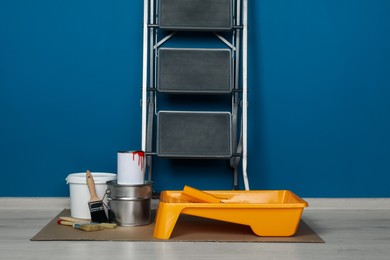 Metallic folding ladder and painting tools near blue wall indoors