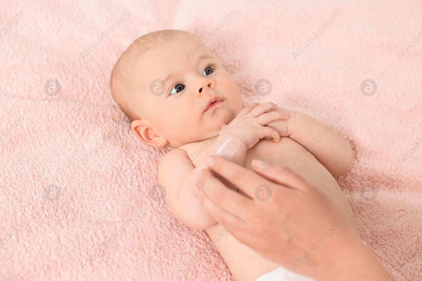 Photo of Woman applying body cream onto baby`s skin on bed, closeup