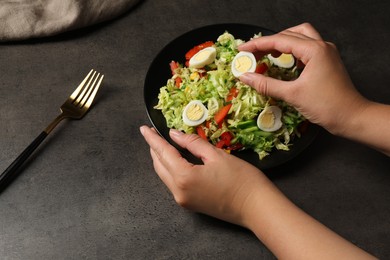 Photo of Woman making delicious salad with Chinese cabbage and quail eggs at black table, closeup