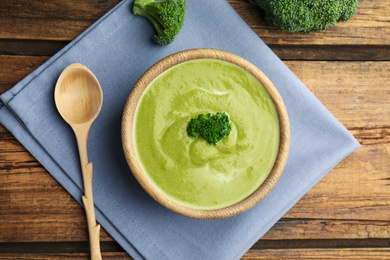 Photo of Delicious broccoli cream soup served on wooden table, flat lay