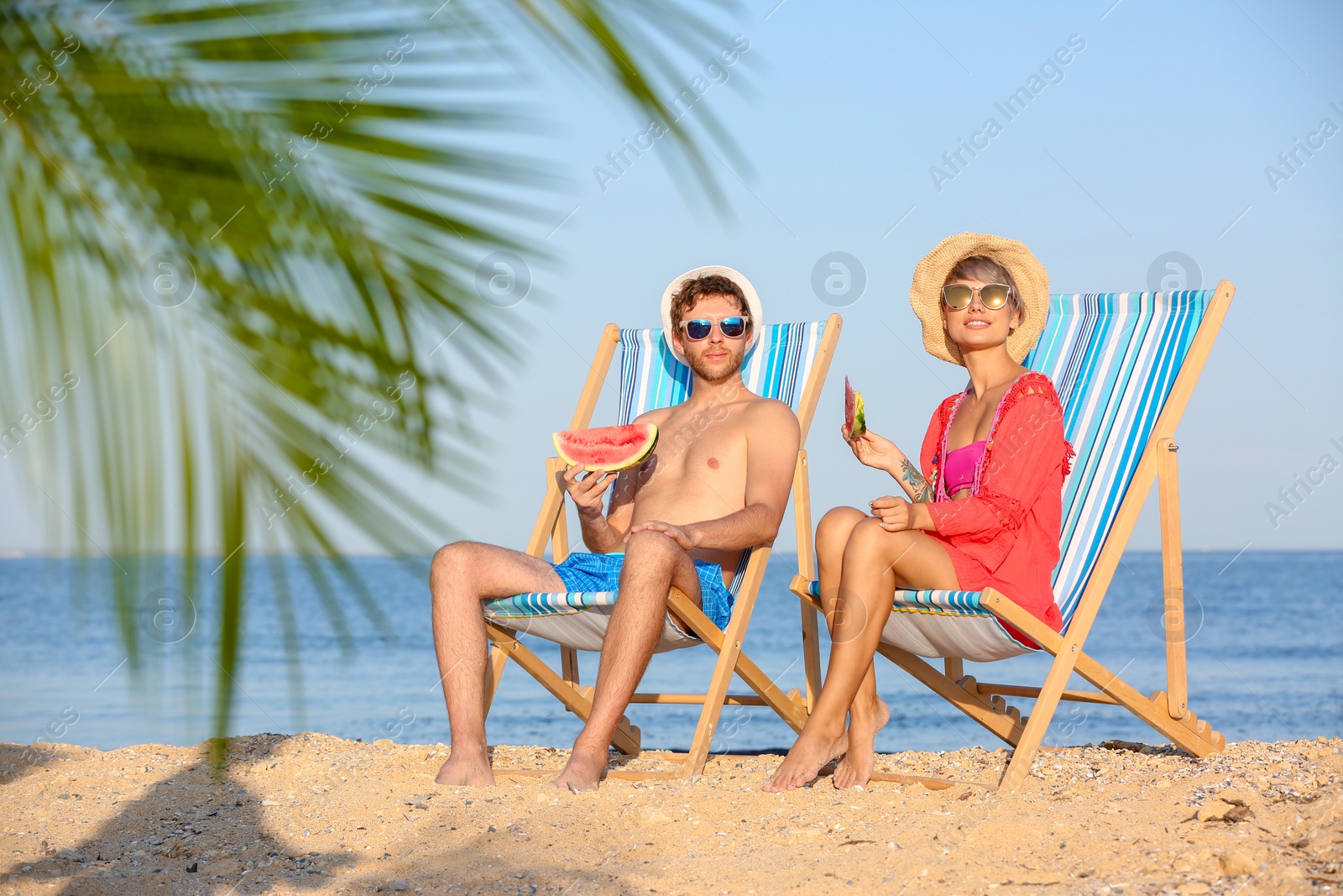 Photo of Young couple with watermelon slices in beach chairs at seacoast