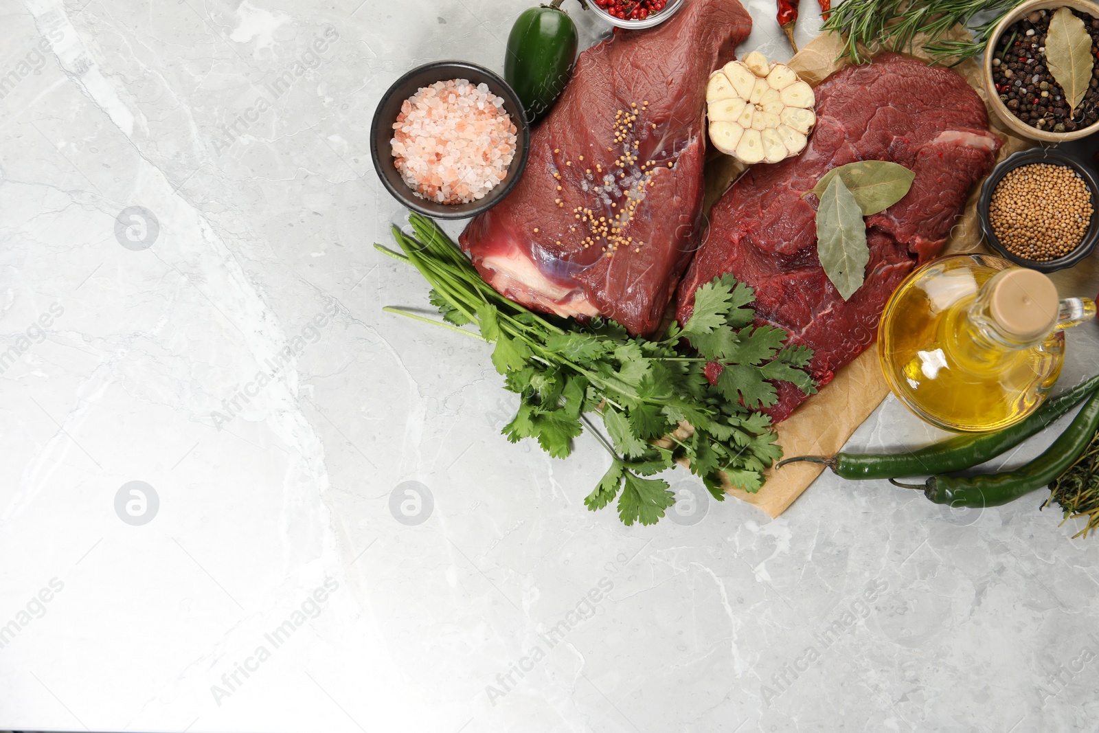 Photo of Pieces of raw beef meat, herbs and spices on light grey marble table, flat lay. Space for text