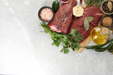 Pieces of raw beef meat, herbs and spices on light grey marble table, flat lay. Space for text