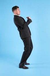 Emotional man in suit pointing at himself on light blue background