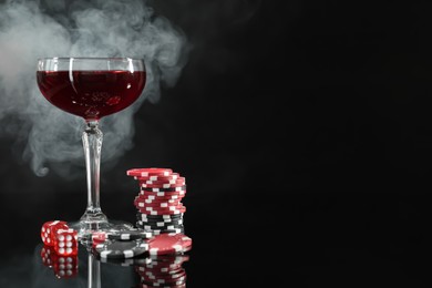 Photo of Casino chips, dice and glass of wine on dark background with smoke. Space for text