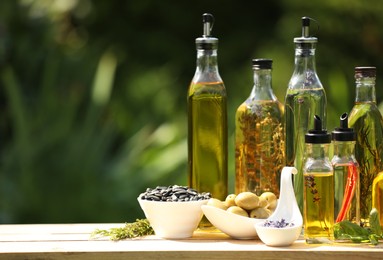 Different cooking oils and ingredients on wooden table against blurred green background. Space for text