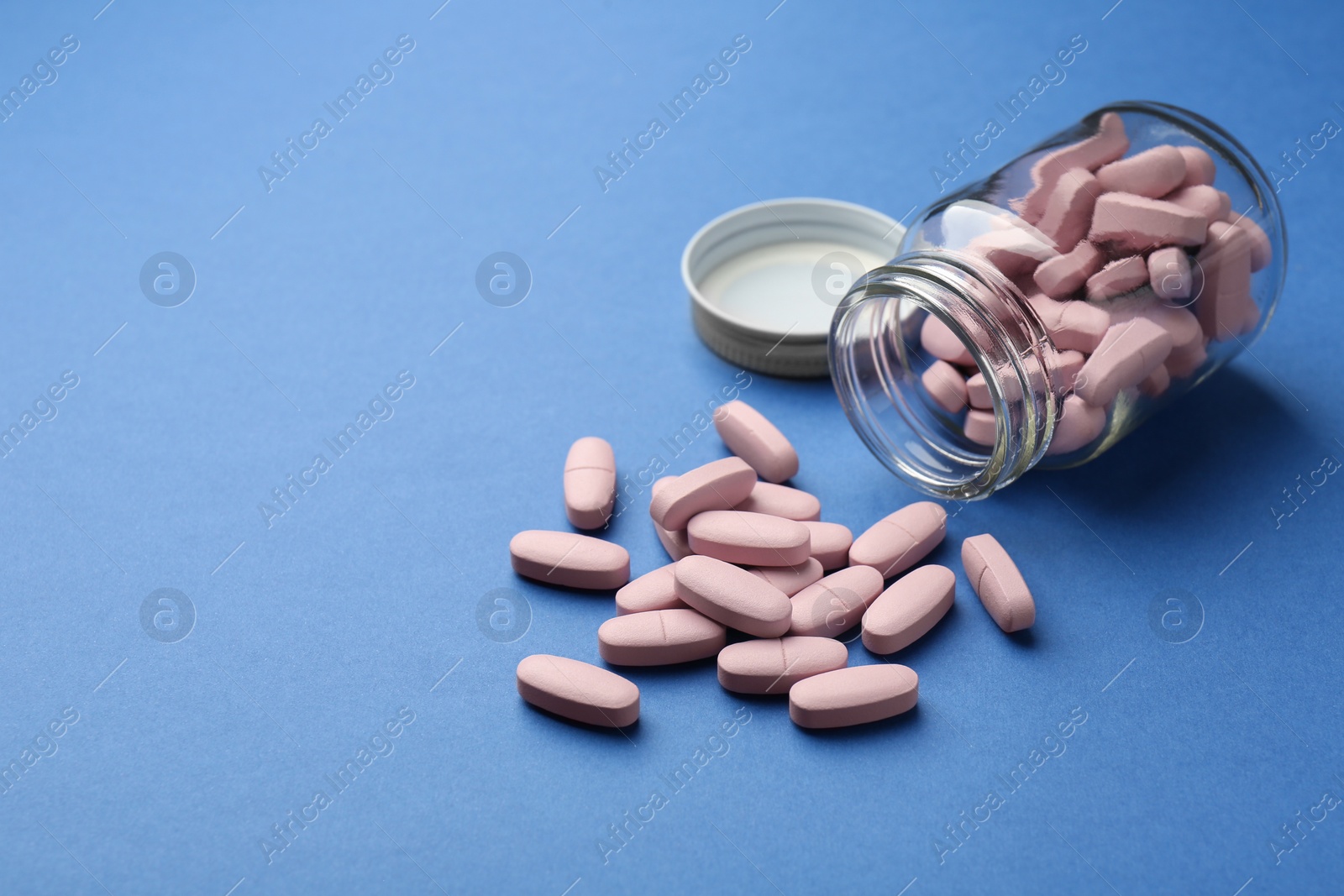 Photo of Bottle of pink vitamin capsules on blue background, space for text