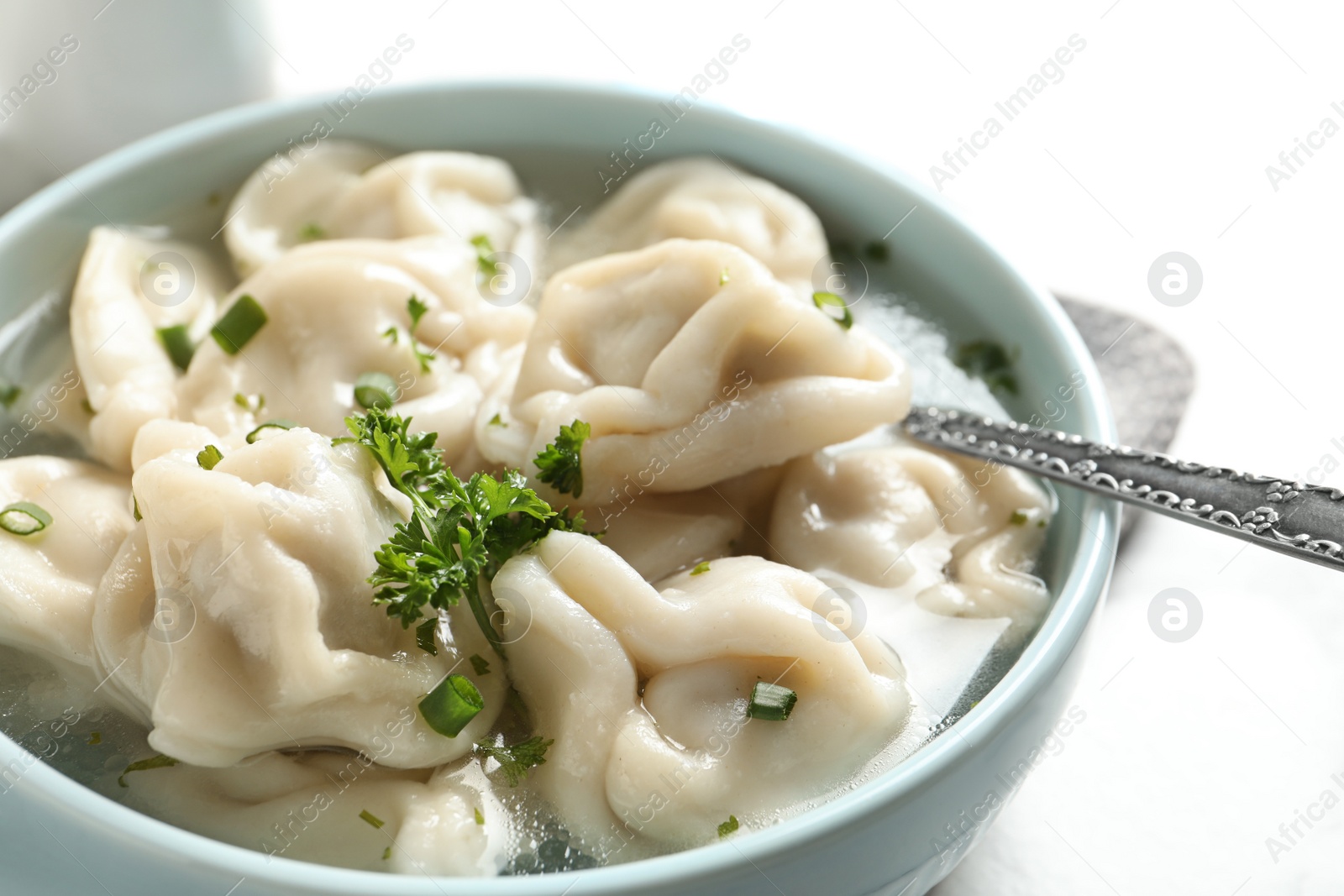 Photo of Bowl of tasty dumplings in broth with spoon on table, closeup