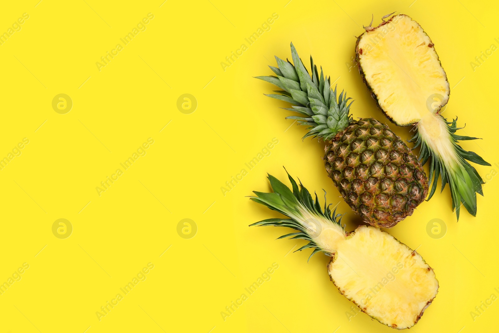 Photo of Whole and cut ripe pineapples on yellow background, flat lay. Space for text