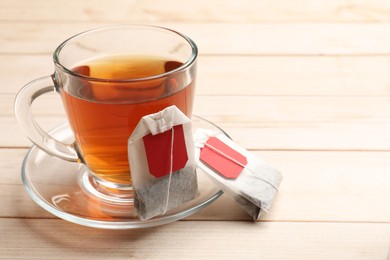 Photo of Tea bags and glass cup of hot beverage on light wooden table, closeup. Space for text