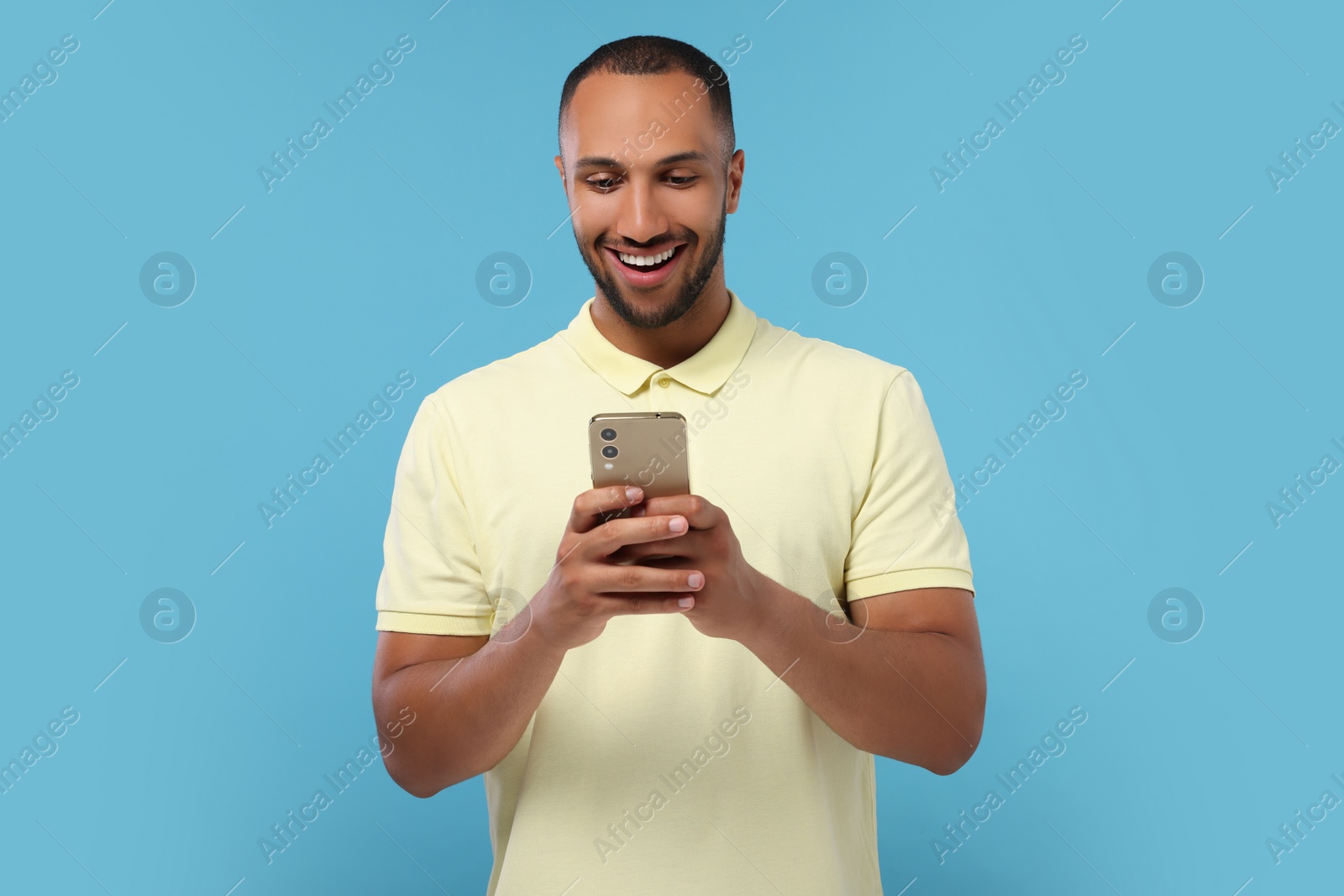 Photo of Happy man sending message via smartphone on light blue background