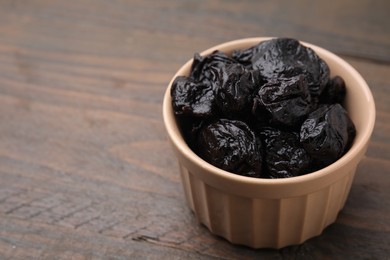 Photo of Sweet dried prunes in bowl on wooden table, closeup. Space for text