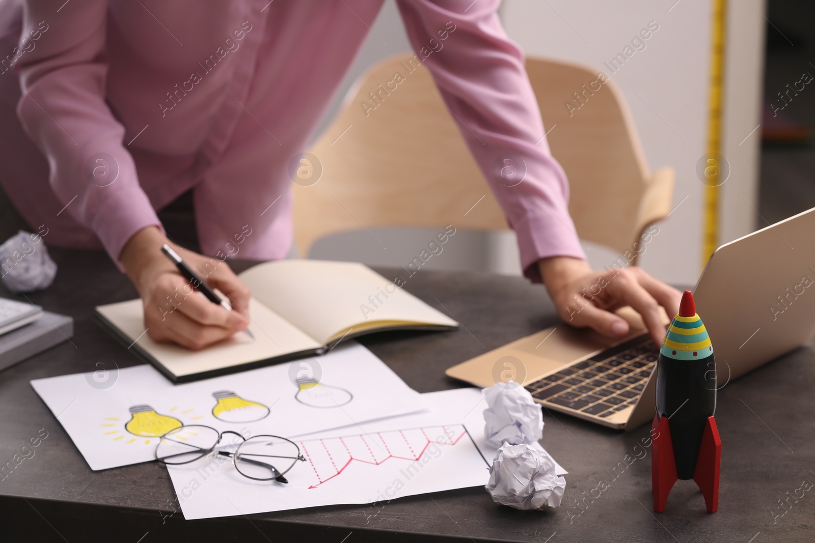 Photo of Woman working at messy table, focus on toy rocket. Startup concept