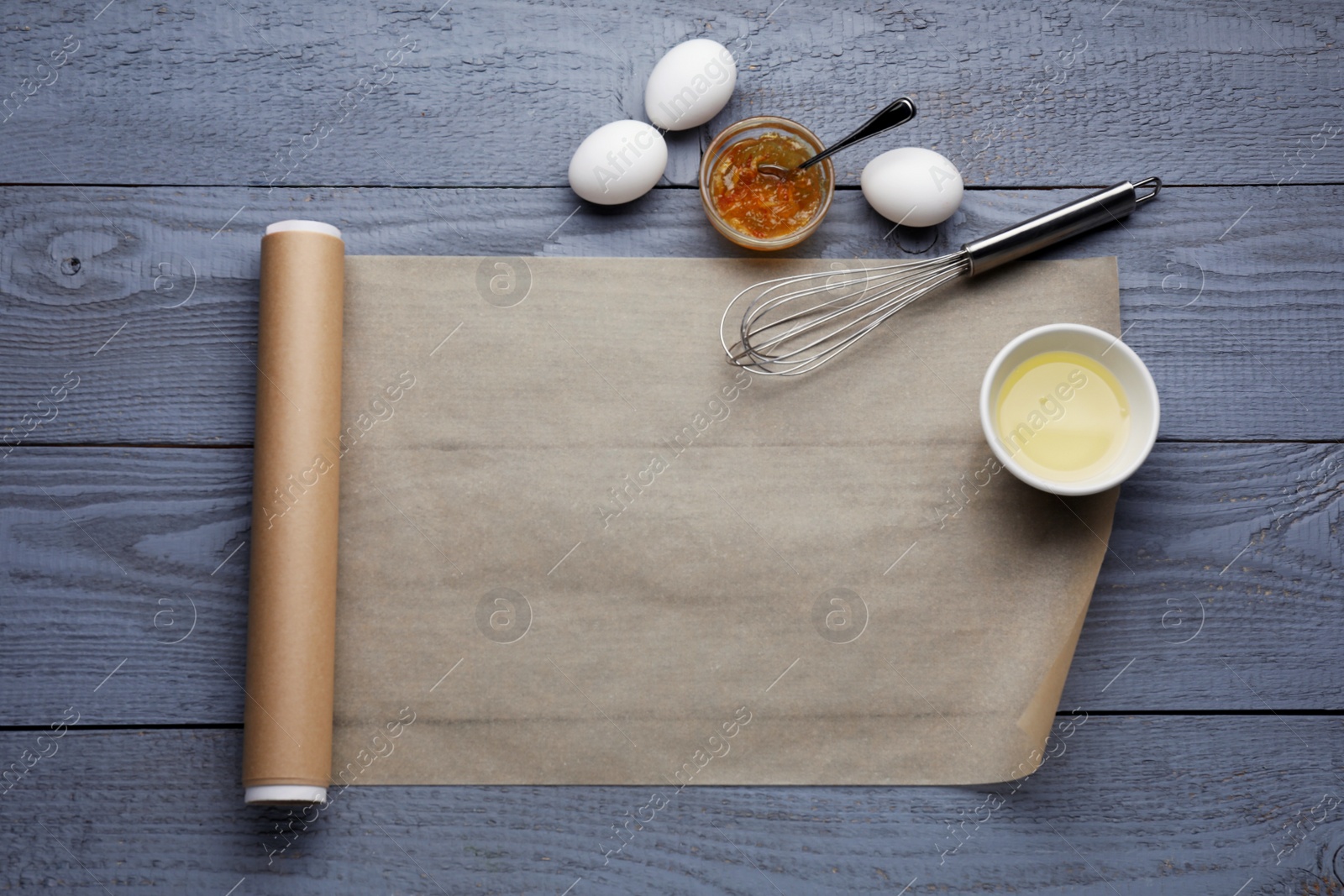 Photo of Baking parchment paper and ingredients on grey wooden table, flat lay. Space for text