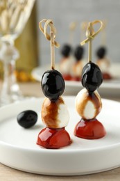 Tasty canapes with black olives, mozzarella and cherry tomatoes on light wooden table, closeup