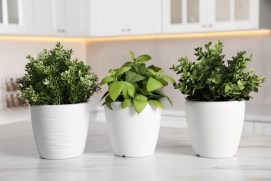 Photo of Artificial potted herbs on white marble table in kitchen. Home decor