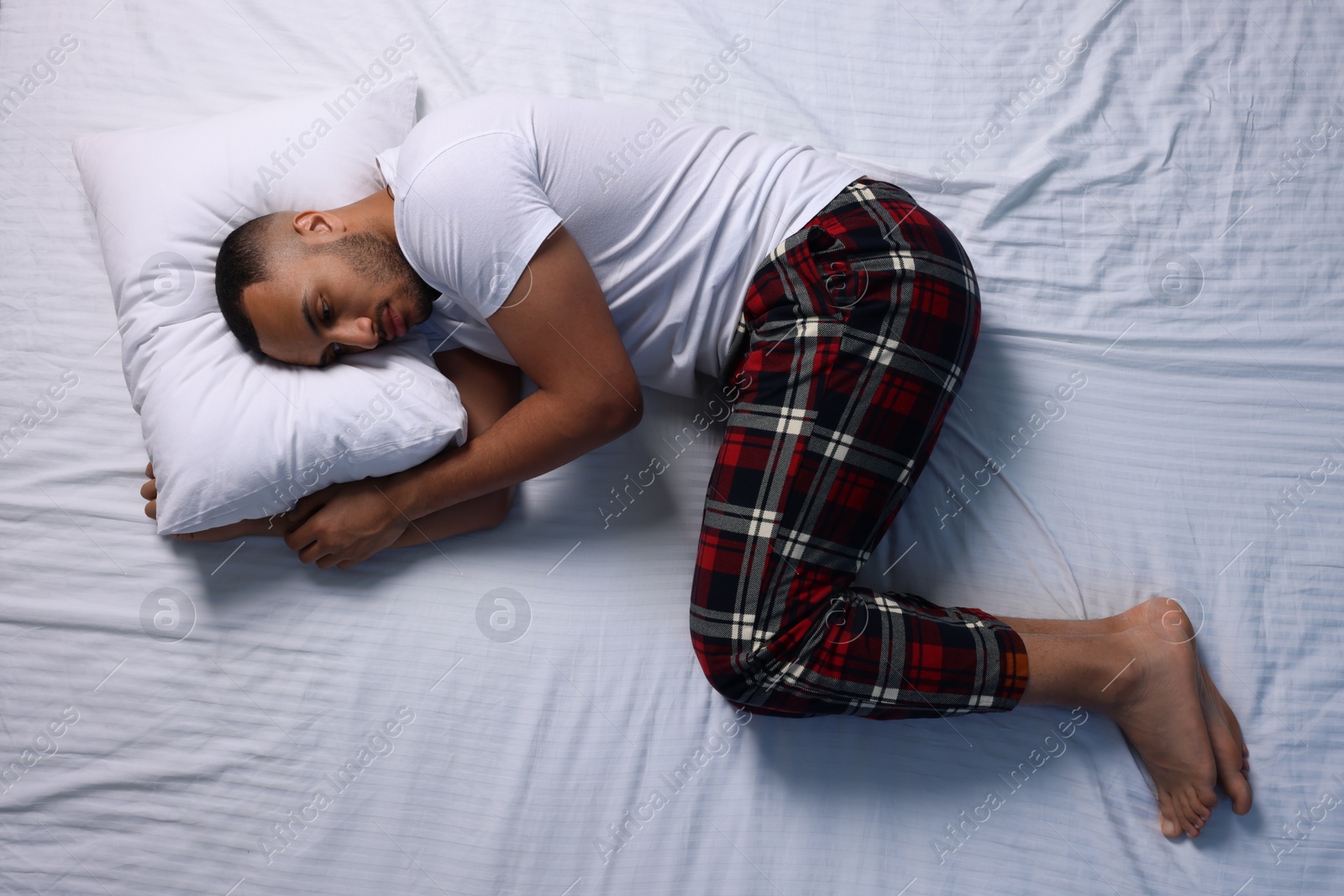 Photo of Man suffering from insomnia on bed, top view