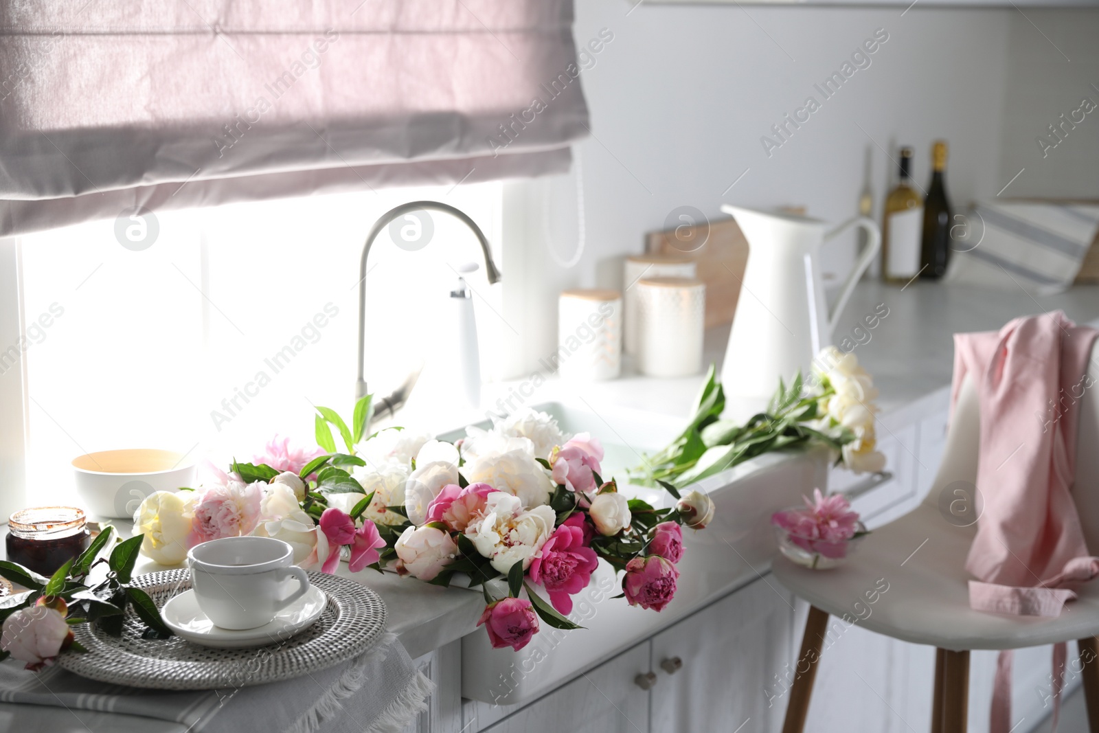 Photo of Beautiful peonies and cup of tea on kitchen counter