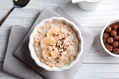 Photo of Quinoa porridge with banana and nuts in bowl served for breakfast on white wooden table, top view