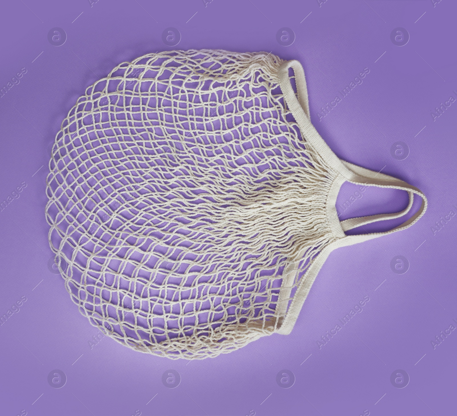 Photo of Empty white net bag on lilac background, top view