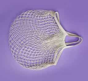 Empty white net bag on lilac background, top view