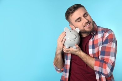 Happy young man with piggy bank and space for text on color background. Money saving