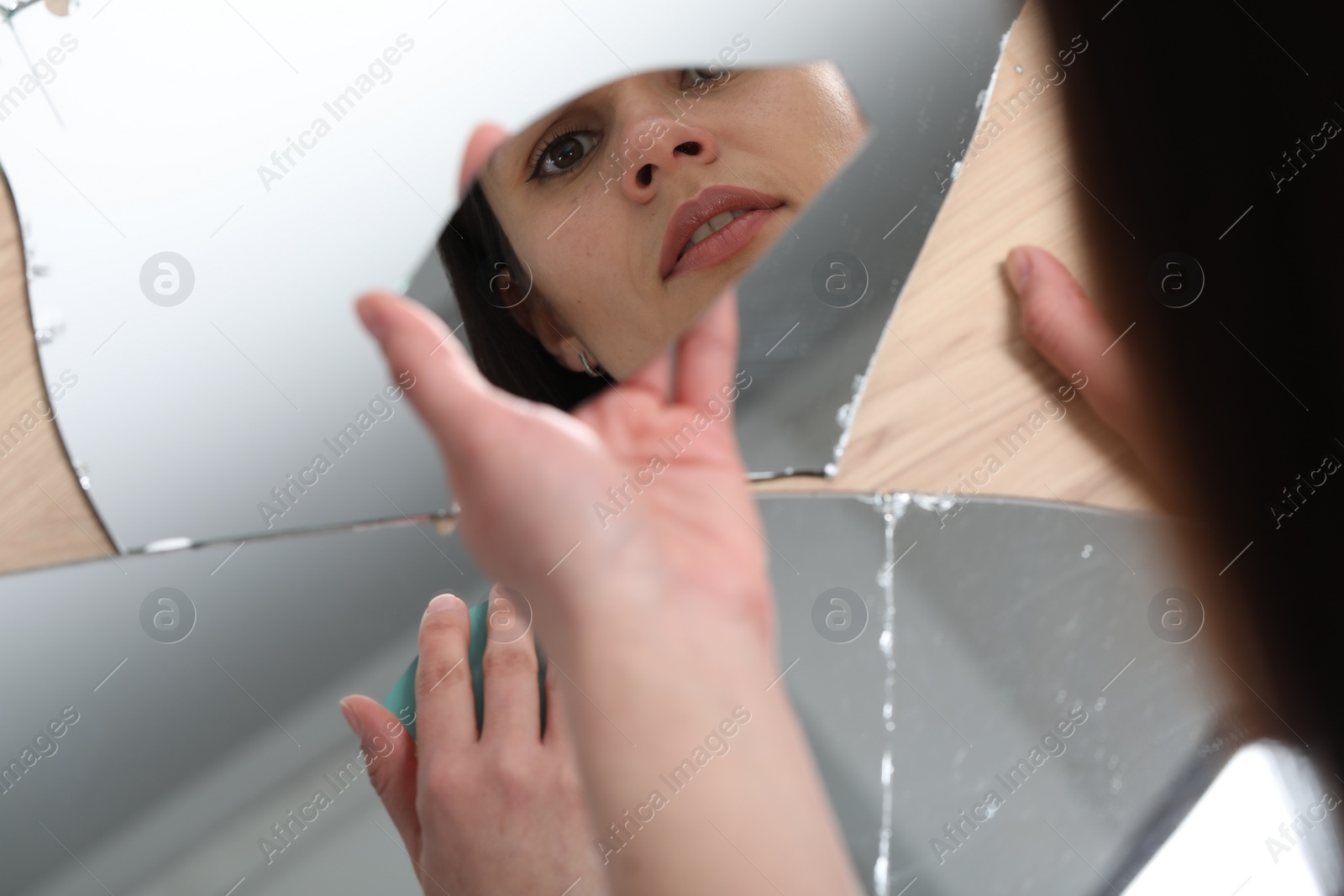 Photo of Young woman looking at herself in shard of broken mirror on background, closeup