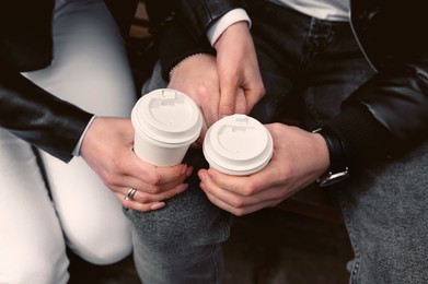 Photo of Lovely couple with coffee holding hands together while sitting on bench outdoors, closeup. Romantic date