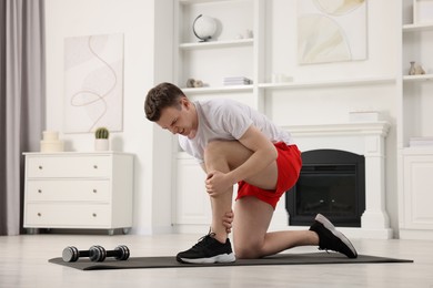 Photo of Man suffering from leg pain on mat at home