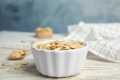 Photo of Bowl of raw pumpkin seeds on white wooden table