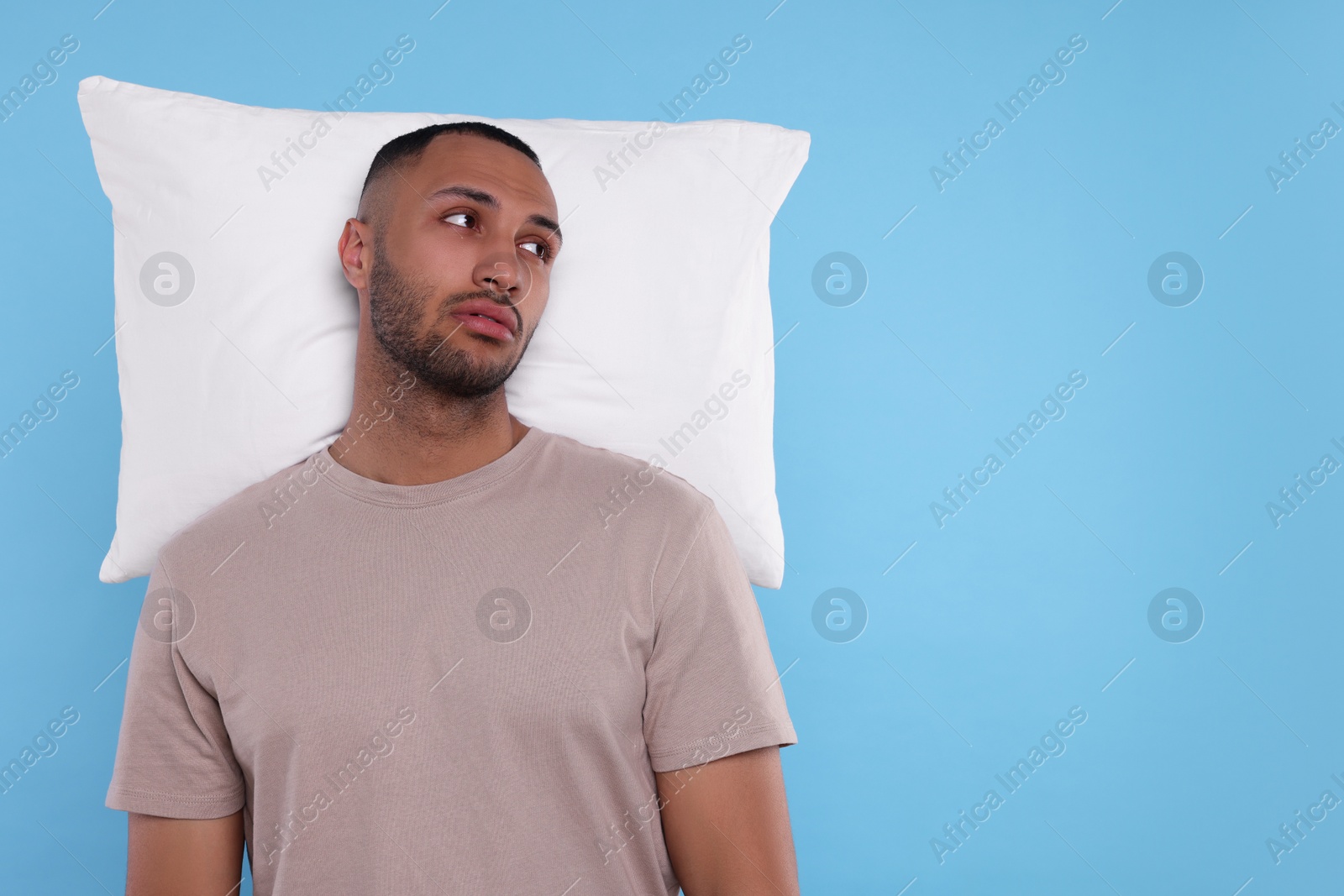 Photo of Tired man with pillow on light blue background, space for text. Insomnia problem