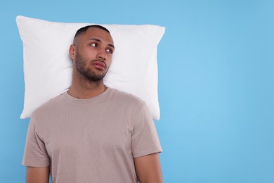Photo of Tired man with pillow on light blue background, space for text. Insomnia problem