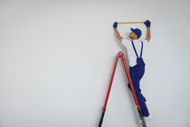 Photo of Construction worker using measuring tape indoors. Room renovation