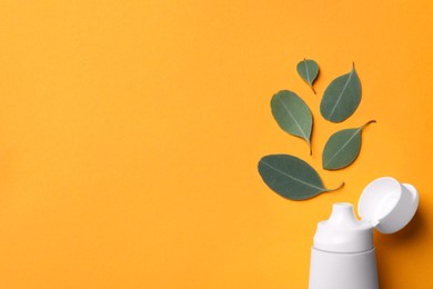 Photo of Blank tube of toothpaste and eucalyptus leaves on orange background, flat lay. Space for text