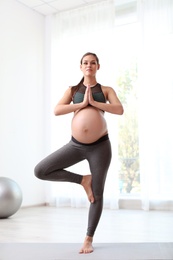 Photo of Young pregnant woman in fitness clothes practicing yoga at home