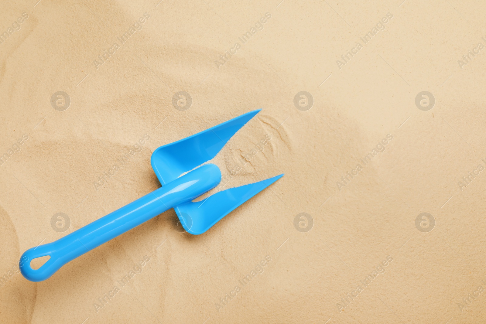 Photo of Bright plastic toy shovel on sand, top view