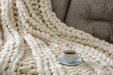 Cup of drink on couch with soft knitted blanket in room, closeup. Interior element