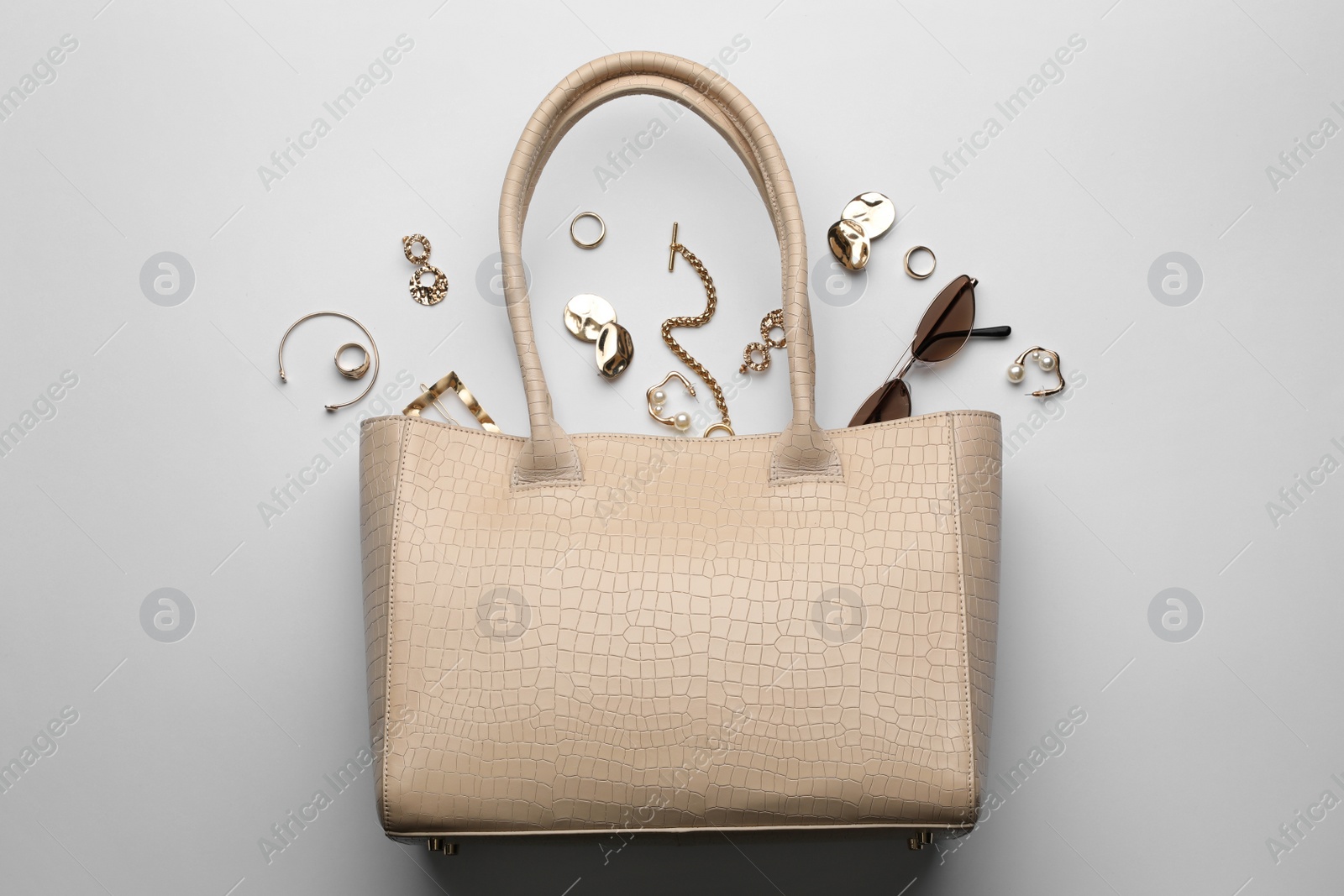 Photo of Stylish woman's bag, sunglasses and bijouterie on light background, flat lay