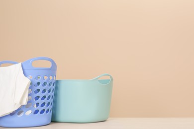Photo of Plastic laundry baskets with clothes near beige wall. Space for text