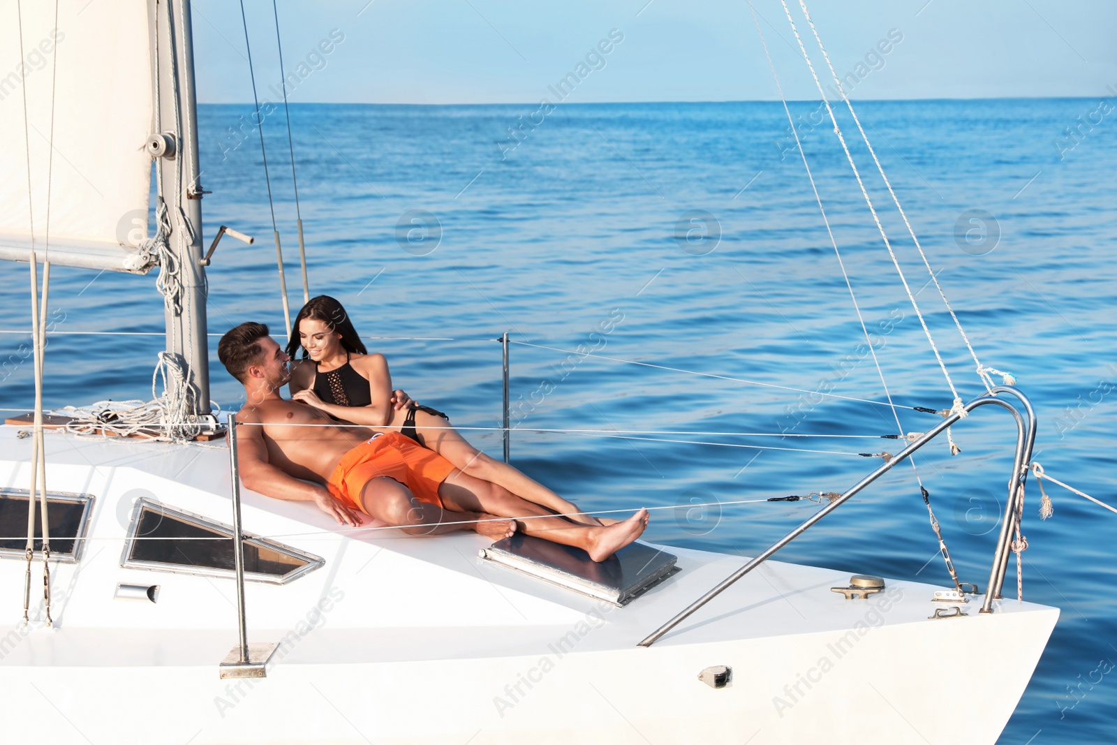 Photo of Young man and his beautiful girlfriend in bikini relaxing on yacht. Happy couple at sea