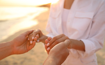 Lovely couple holding hands on beach at sunset, closeup