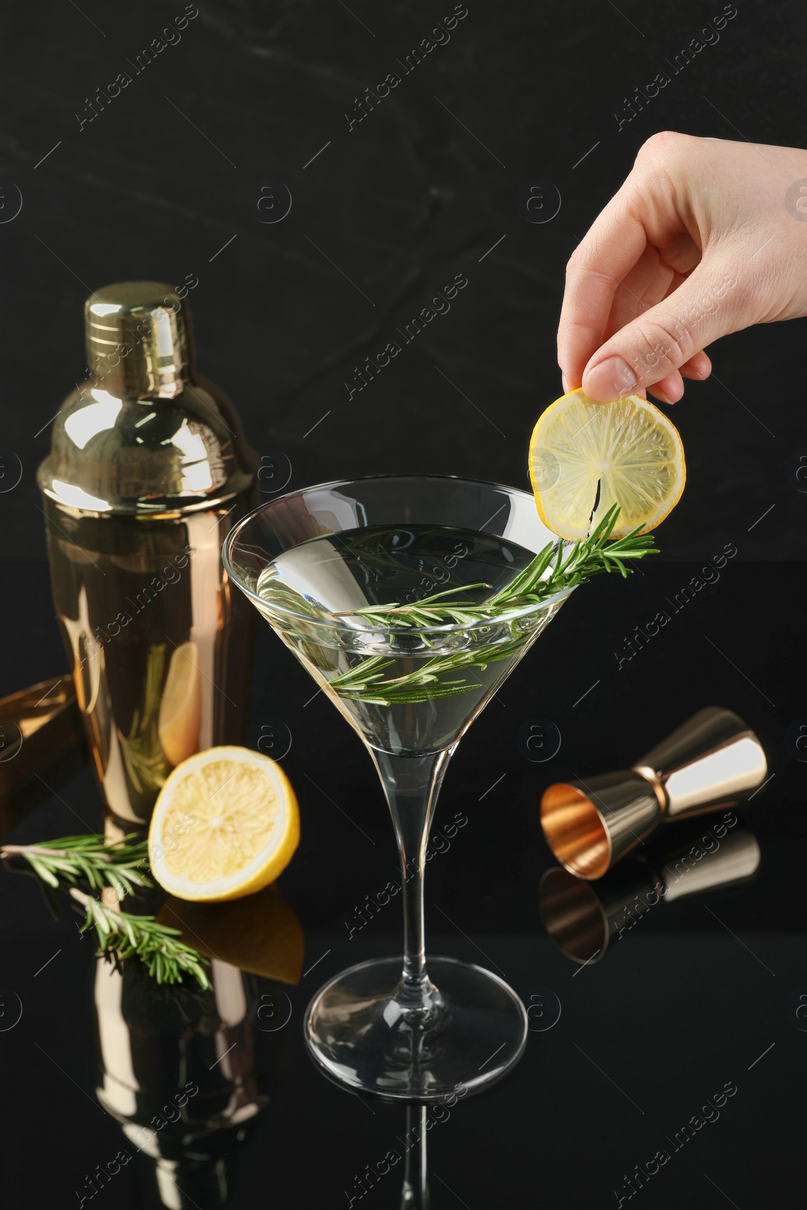 Photo of Woman decorating Martini cocktail with lemon slice on black background, closeup